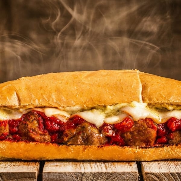 Steaming hot meatball sub with melted cheese and red sauce on a wooden surface.